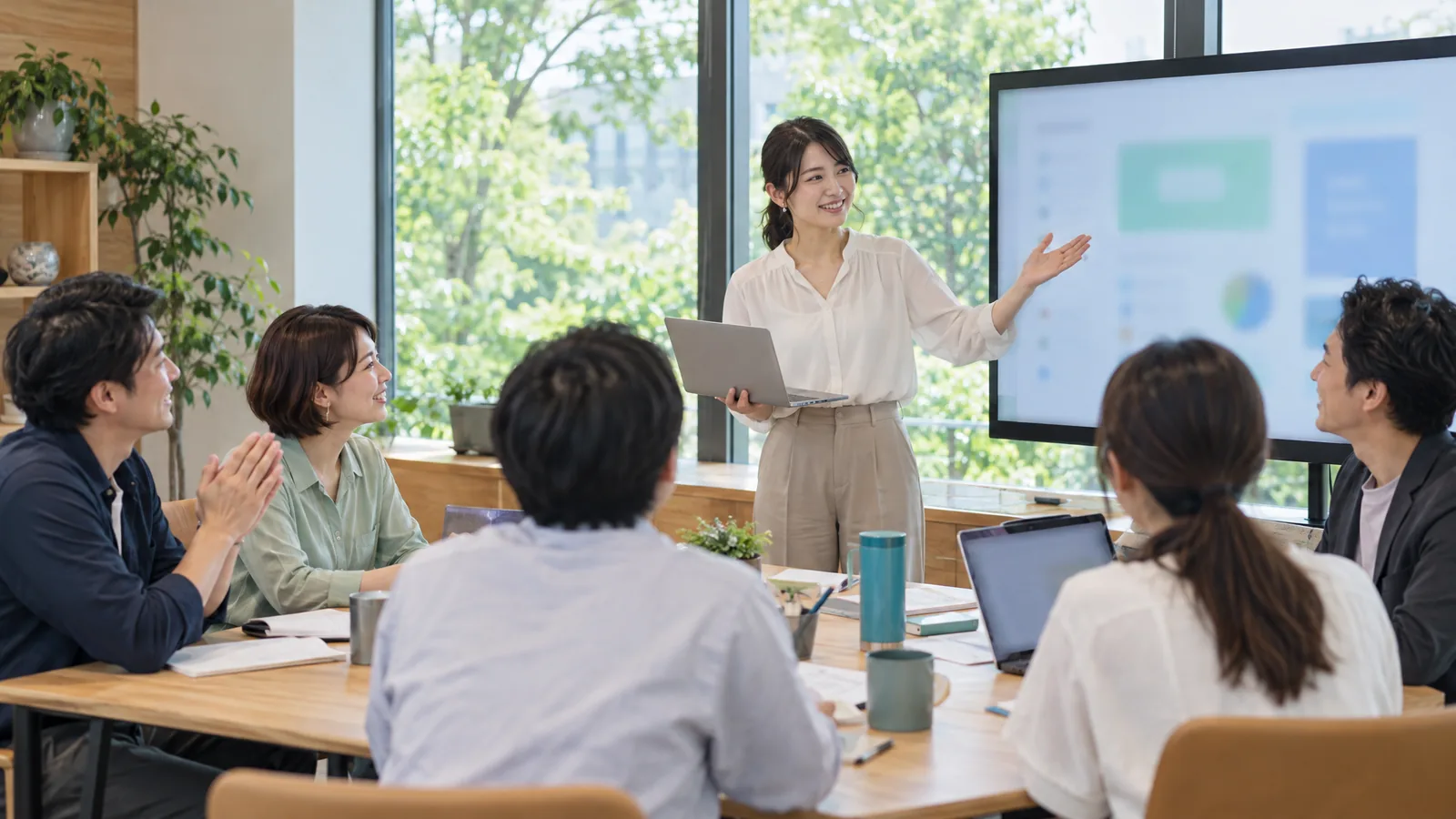受講者が大きな画面の前で自分の作ったツールを発表し、同僚が聞いている様子