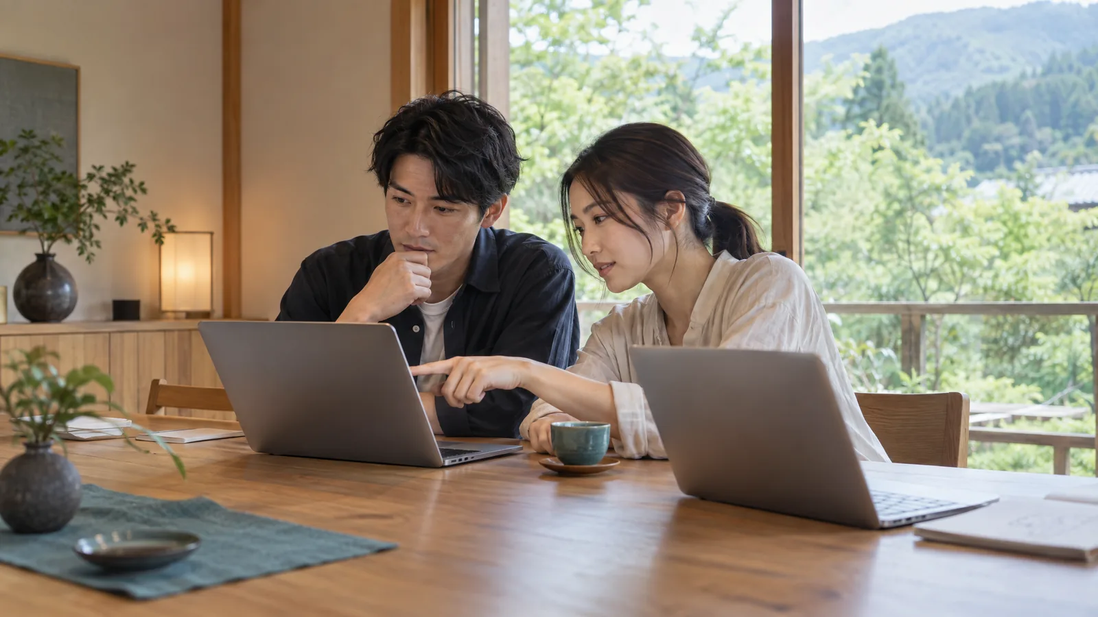 木々の見える静かな会議室で、2人の社員が並んでノートPCの作業に集中している様子